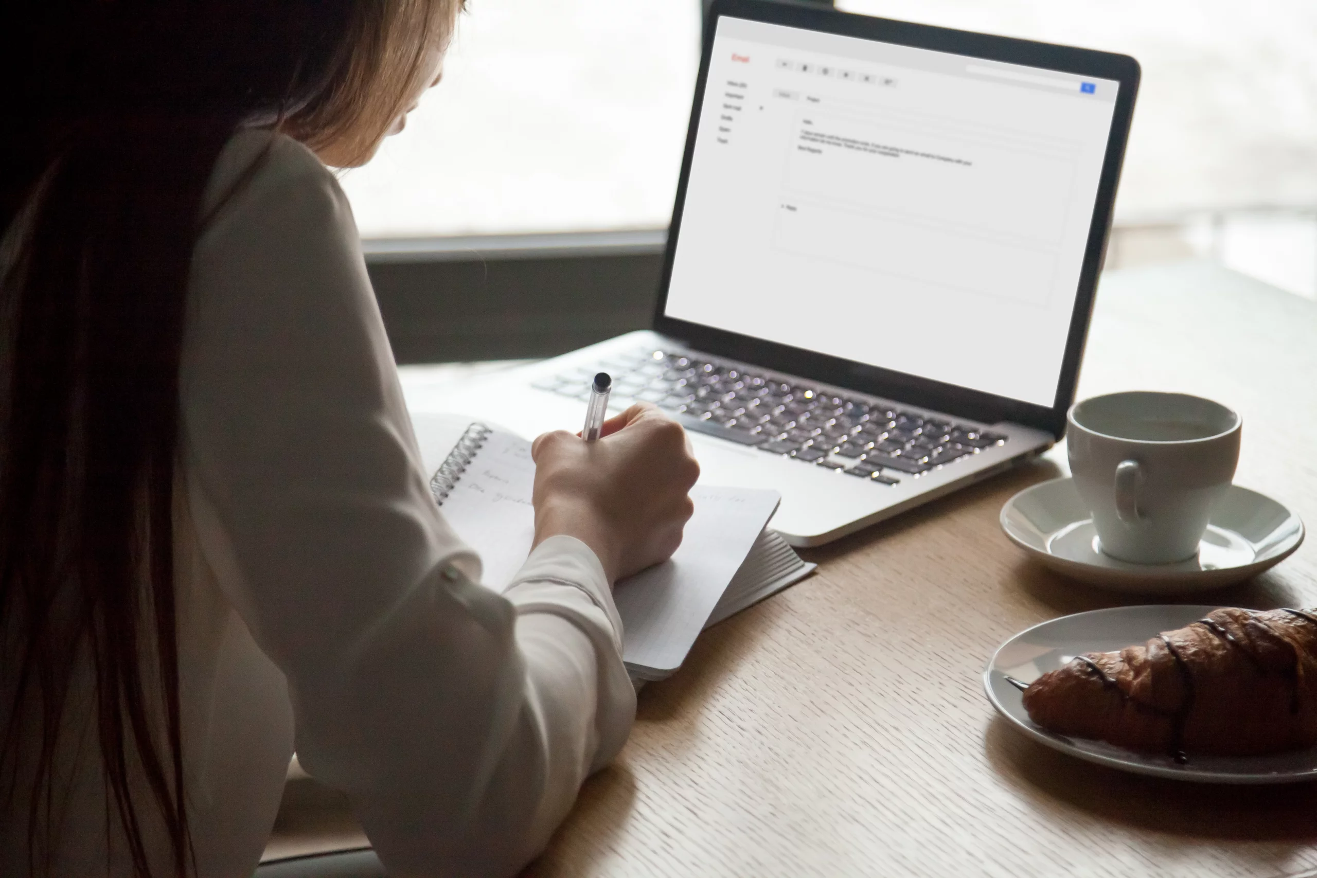 Woman making notes reading email letter on laptop in cafe